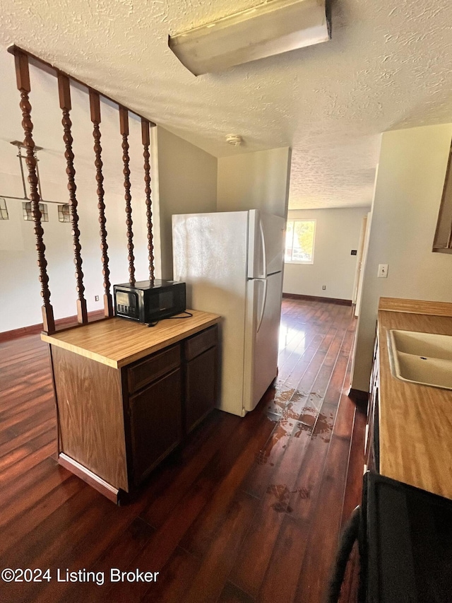 kitchen featuring dark hardwood / wood-style floors, sink, wooden counters, white fridge, and a textured ceiling