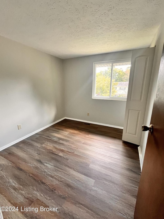 empty room with dark hardwood / wood-style flooring and a textured ceiling