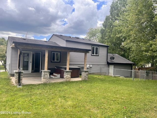 rear view of house with a hot tub, a patio, and a yard