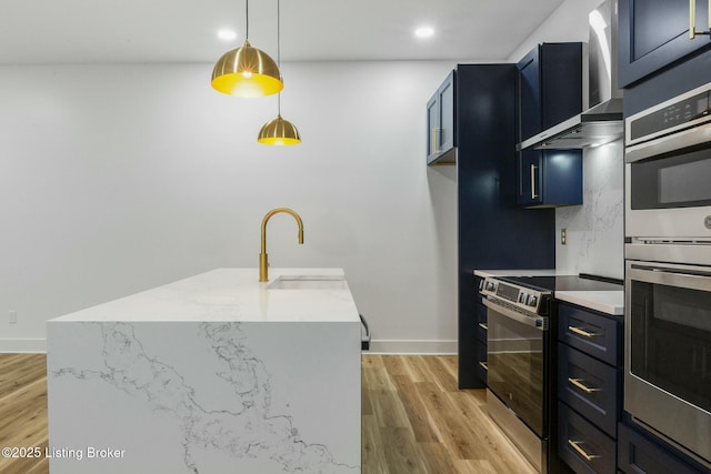 kitchen featuring wall chimney exhaust hood, decorative light fixtures, light hardwood / wood-style flooring, stainless steel appliances, and a kitchen island with sink