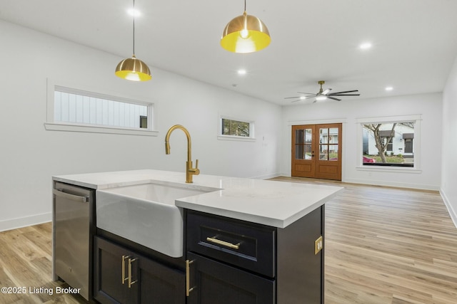 kitchen with pendant lighting, dishwasher, an island with sink, sink, and light hardwood / wood-style flooring