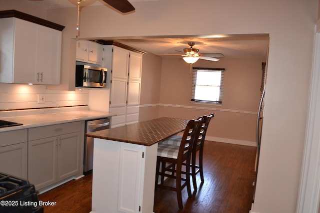 kitchen with ceiling fan, appliances with stainless steel finishes, a kitchen breakfast bar, a center island, and white cabinets