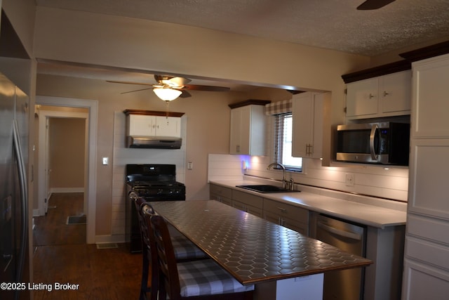 kitchen with sink, a textured ceiling, appliances with stainless steel finishes, dark hardwood / wood-style flooring, and white cabinets