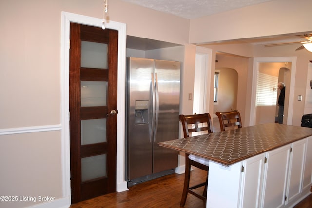 kitchen featuring dark wood-type flooring, stainless steel fridge, a kitchen breakfast bar, ceiling fan, and white cabinets