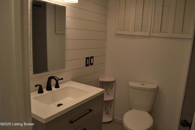 bathroom featuring wooden walls, vanity, and toilet