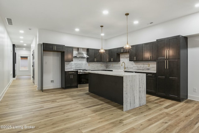 kitchen featuring hanging light fixtures, wall chimney range hood, stainless steel range with electric cooktop, and light hardwood / wood-style floors