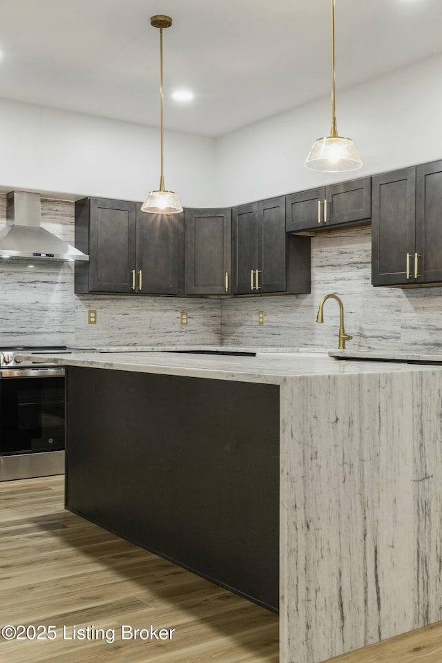 kitchen featuring sink, hanging light fixtures, wall chimney exhaust hood, wall oven, and light hardwood / wood-style flooring