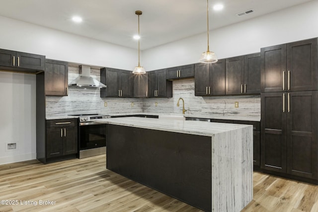 kitchen with wall chimney exhaust hood, light stone counters, stainless steel electric range oven, decorative light fixtures, and light hardwood / wood-style floors