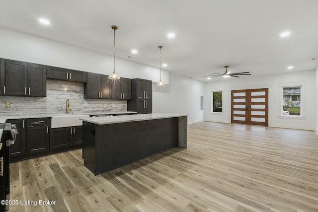 kitchen with sink, decorative backsplash, hanging light fixtures, a center island, and light stone counters