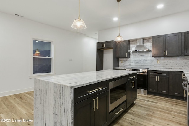 kitchen with decorative light fixtures, a center island, stainless steel appliances, wall chimney range hood, and light wood-type flooring