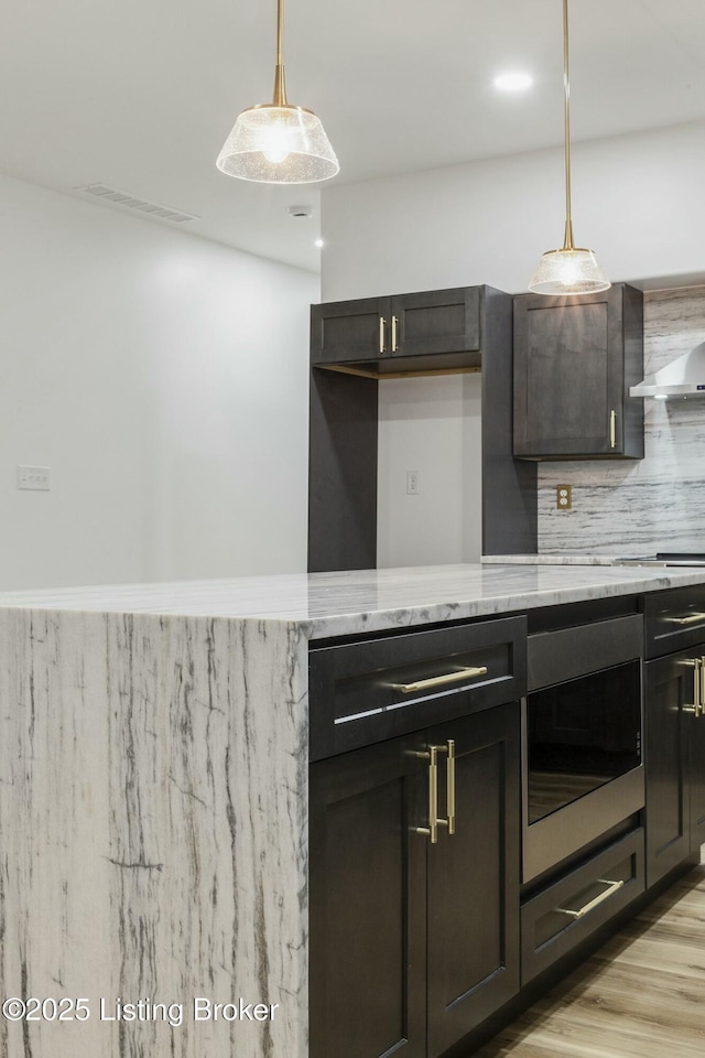 kitchen with light stone counters, decorative backsplash, built in microwave, decorative light fixtures, and light wood-type flooring