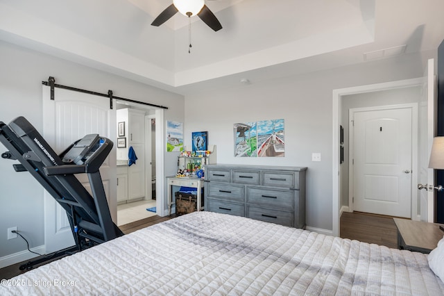 bedroom with ceiling fan, a barn door, a raised ceiling, and light hardwood / wood-style flooring