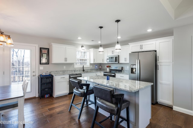 kitchen with white cabinetry, hanging light fixtures, stainless steel appliances, dark hardwood / wood-style floors, and a kitchen island