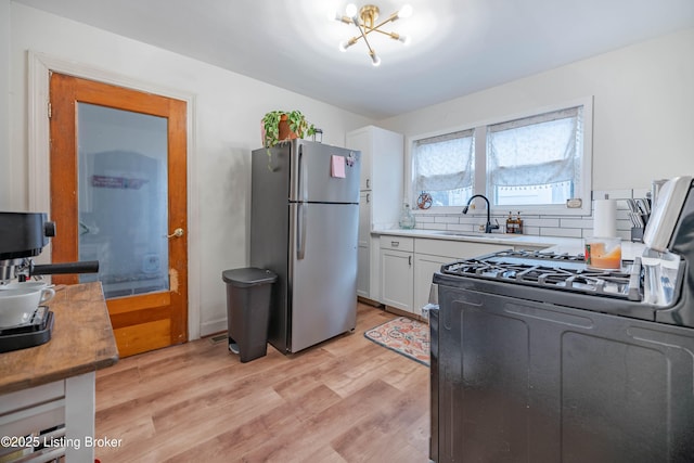 kitchen featuring stainless steel refrigerator, white cabinetry, sink, light hardwood / wood-style floors, and gas stove