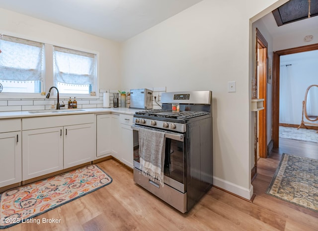 kitchen with stainless steel gas stove, sink, white cabinets, and light wood-type flooring