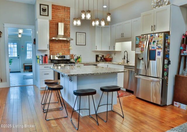 kitchen featuring sink, a kitchen island, pendant lighting, stainless steel appliances, and wall chimney range hood