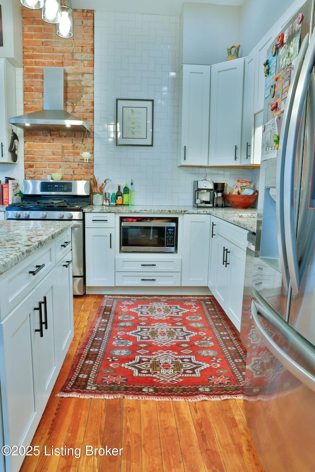 kitchen featuring white cabinetry, wall chimney range hood, light hardwood / wood-style floors, and appliances with stainless steel finishes