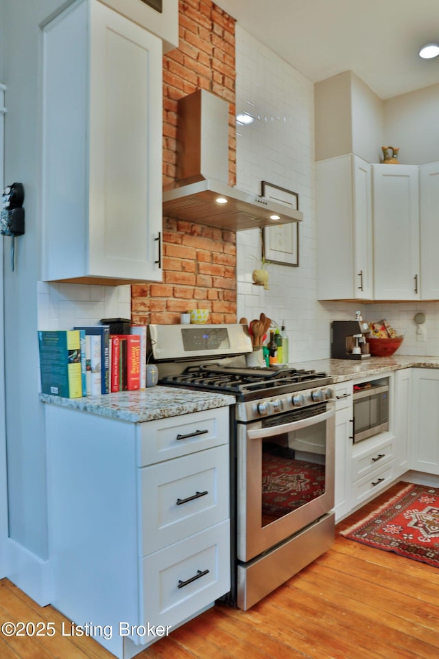 kitchen with white cabinetry, appliances with stainless steel finishes, light hardwood / wood-style floors, and wall chimney exhaust hood