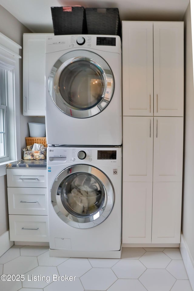 laundry area with light tile patterned flooring, cabinets, and stacked washer / dryer