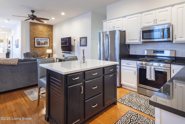 kitchen featuring appliances with stainless steel finishes, tasteful backsplash, light hardwood / wood-style floors, white cabinets, and a kitchen island