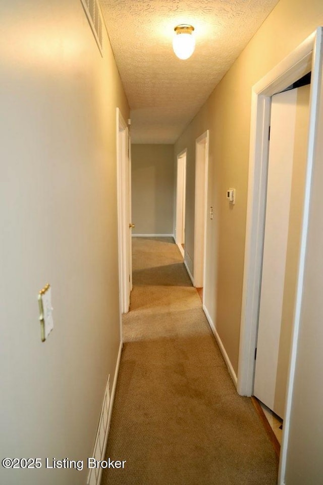 hallway featuring a textured ceiling, baseboards, visible vents, and light colored carpet