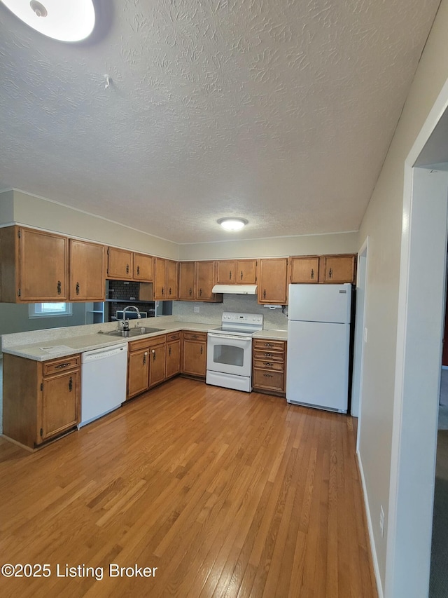 kitchen with white appliances, brown cabinets, light countertops, light wood-style floors, and a sink