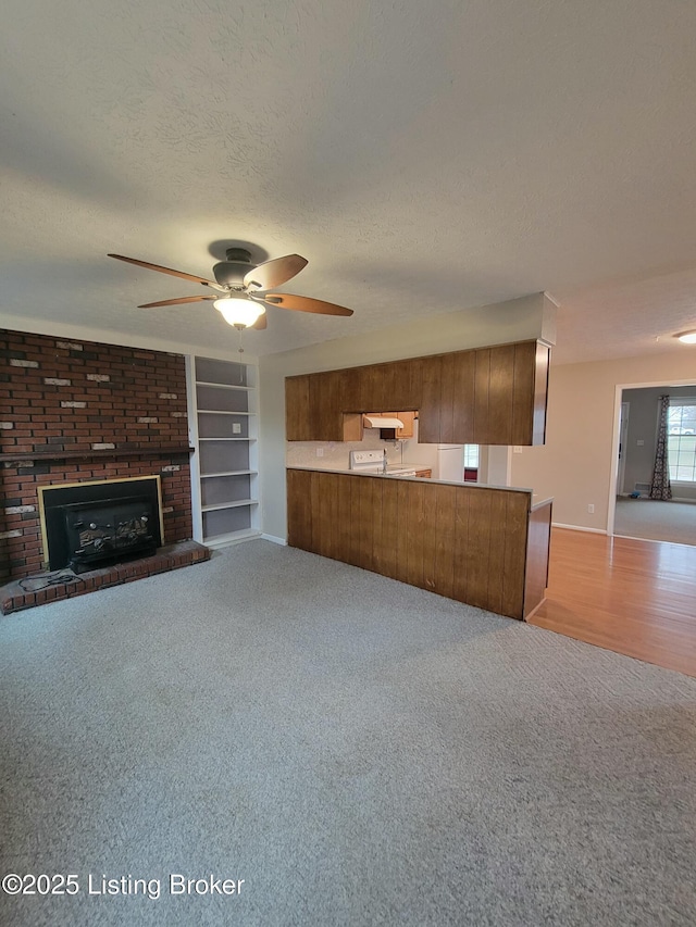 unfurnished living room featuring built in features, a ceiling fan, light colored carpet, a textured ceiling, and a fireplace