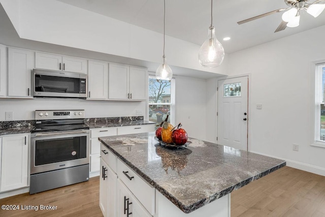 kitchen with dark stone countertops, light wood-type flooring, a kitchen island, stainless steel appliances, and white cabinets