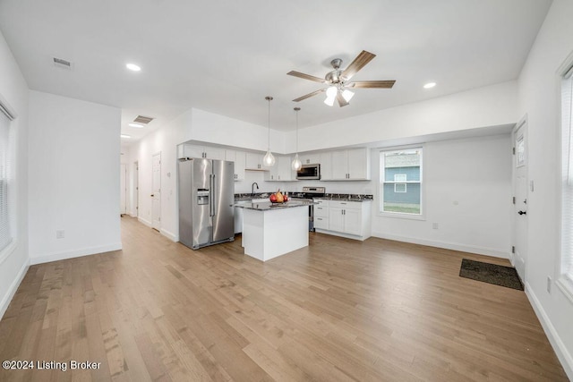 kitchen with appliances with stainless steel finishes, hanging light fixtures, a center island, light hardwood / wood-style floors, and white cabinets