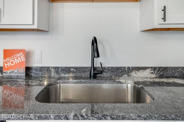 interior details featuring sink, white cabinets, and dark stone counters