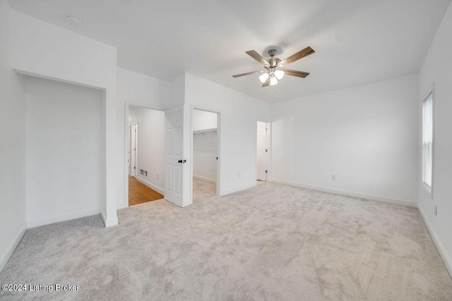 unfurnished bedroom featuring a spacious closet, light colored carpet, a closet, and ceiling fan