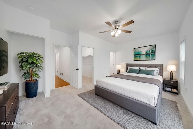 bedroom featuring light carpet, ceiling fan, a spacious closet, and baseboards