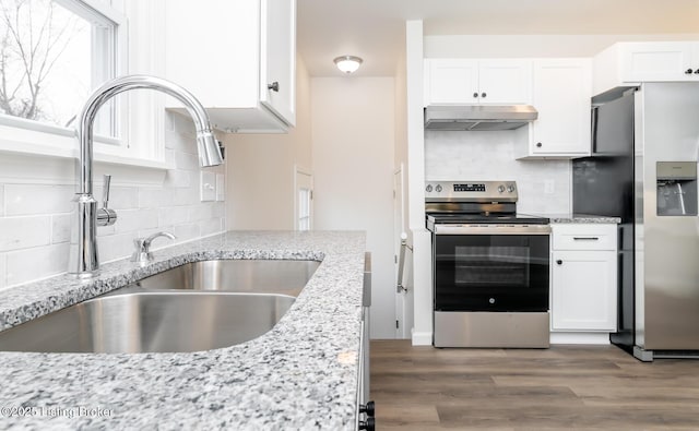 kitchen with sink, appliances with stainless steel finishes, hardwood / wood-style flooring, light stone countertops, and white cabinets