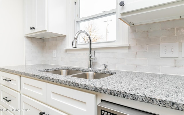 kitchen with dishwasher, sink, white cabinets, backsplash, and light stone counters