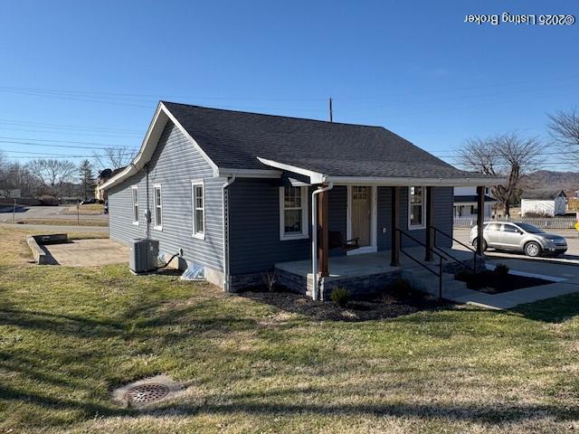 view of front of house featuring a front lawn, cooling unit, a shingled roof, and covered porch