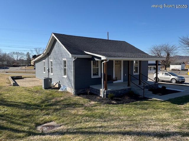 view of front facade featuring central AC, covered porch, and a front yard