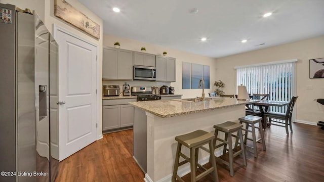 kitchen featuring sink, a breakfast bar area, a kitchen island with sink, gray cabinetry, and stainless steel appliances