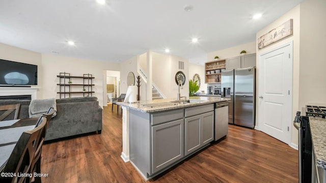 kitchen featuring gray cabinetry, a center island with sink, appliances with stainless steel finishes, dark hardwood / wood-style floors, and light stone countertops