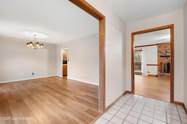 empty room with light wood-type flooring, an inviting chandelier, a textured ceiling, and a fireplace