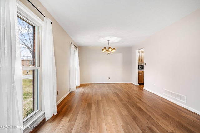 unfurnished room with hardwood / wood-style flooring, a healthy amount of sunlight, and an inviting chandelier