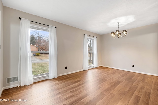 empty room with light hardwood / wood-style floors and a chandelier