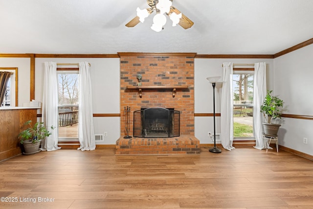 living room with ceiling fan, ornamental molding, a brick fireplace, and light hardwood / wood-style flooring