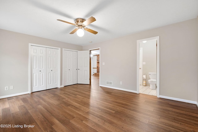 unfurnished bedroom with multiple closets, wood-type flooring, ensuite bathroom, and ceiling fan