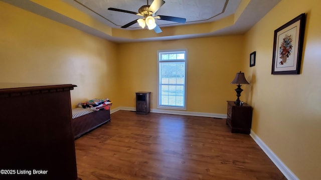 empty room featuring dark wood-type flooring, ceiling fan, and a tray ceiling