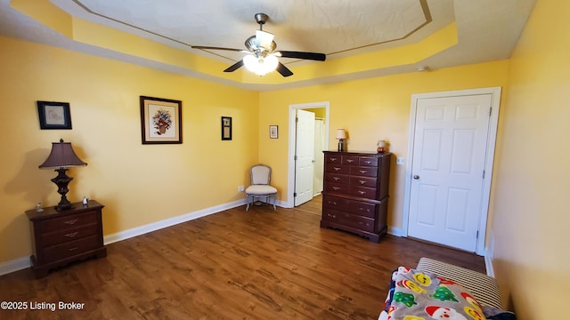 bedroom with a raised ceiling, dark wood-type flooring, and ceiling fan