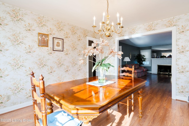 dining space featuring wood-type flooring, a chandelier, and a brick fireplace