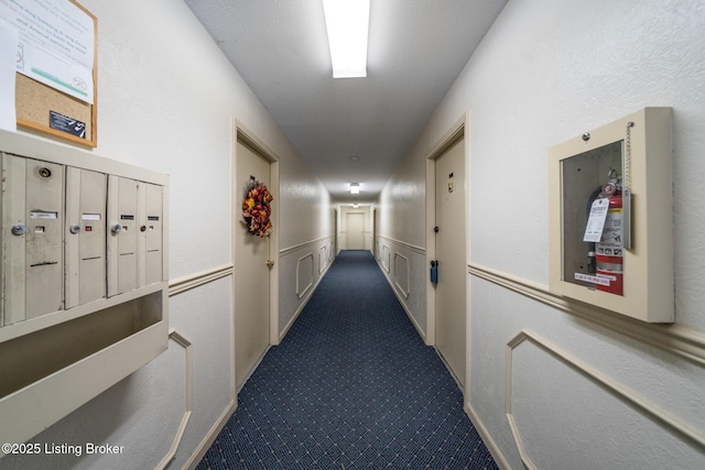 hallway featuring dark colored carpet and a mail area