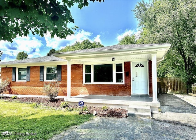 ranch-style house featuring covered porch, brick siding, fence, and driveway