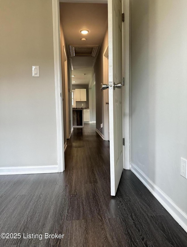 corridor featuring attic access, dark wood-style flooring, and baseboards