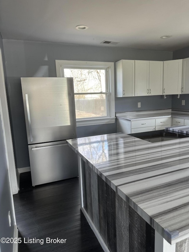 kitchen with dark wood-style floors, light countertops, visible vents, freestanding refrigerator, and white cabinets